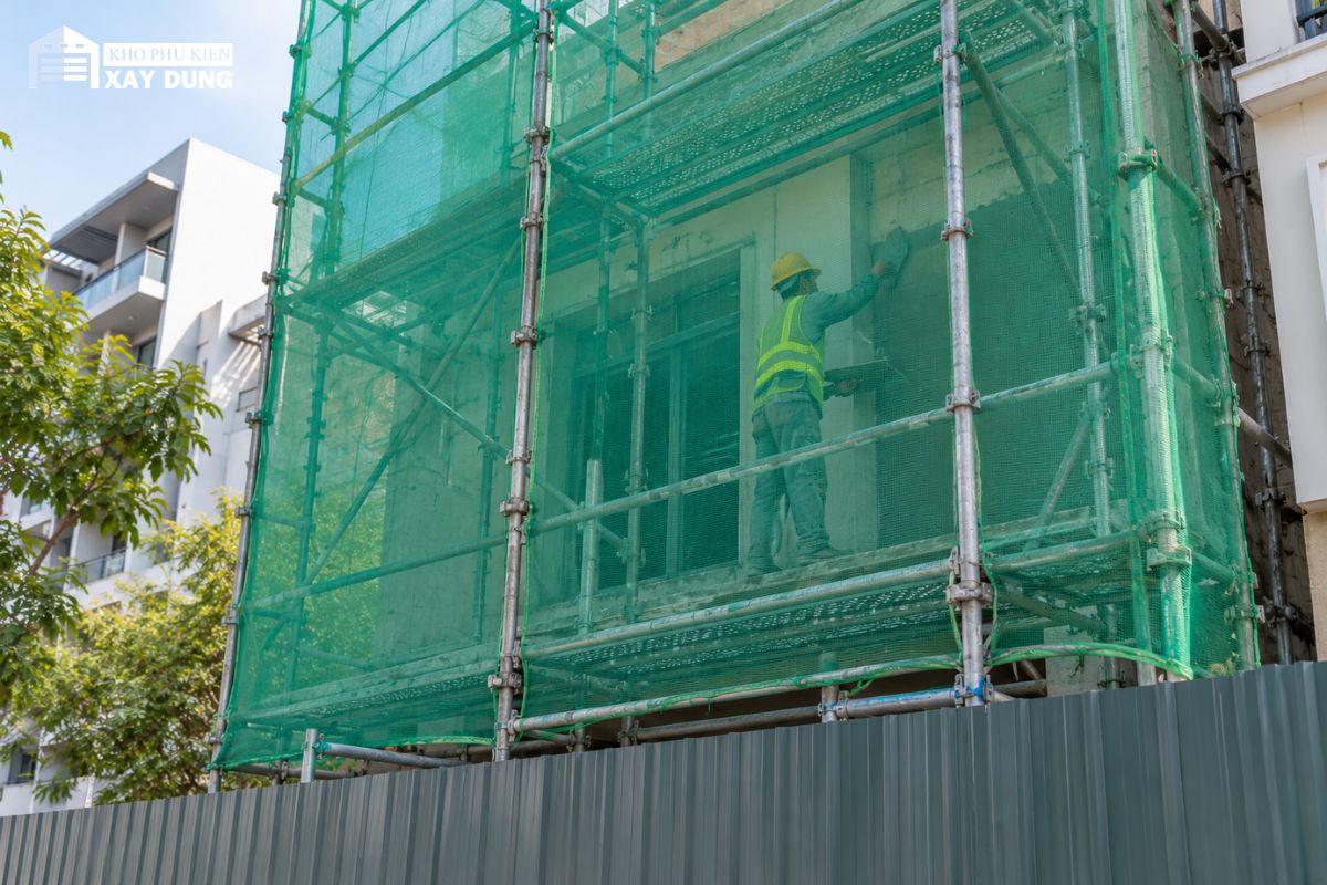 Thợ trát tường sau tấm lưới bao che căng trên giàn giáo nhà phố